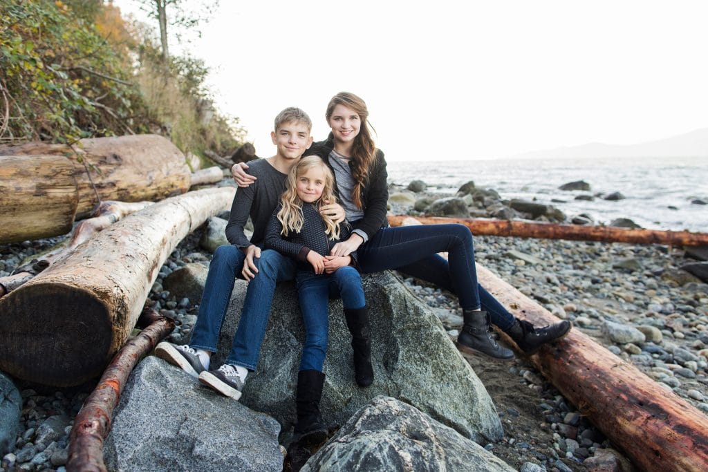 a boy and his 2 sisters sitting on the rocks at Spanish Bank